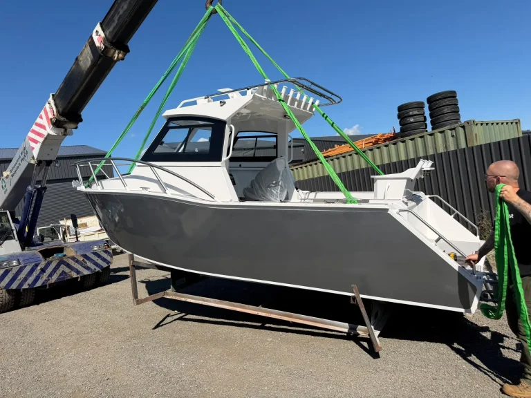 Bare aluminium boat lifted by crane onto a truck