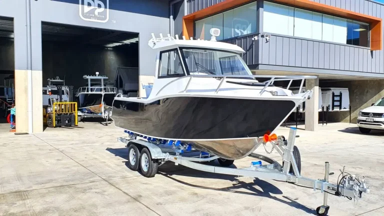 Bare aluminium hardtop boat on a trailer outside the shed