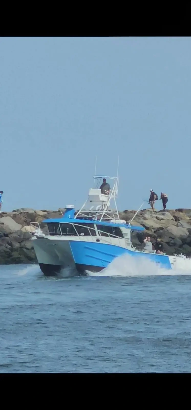 Blue plate aluminium work boat running past a breakwater