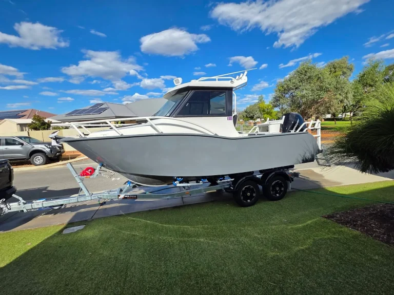 White plate aluminium hardtop boat on a trailer on grass